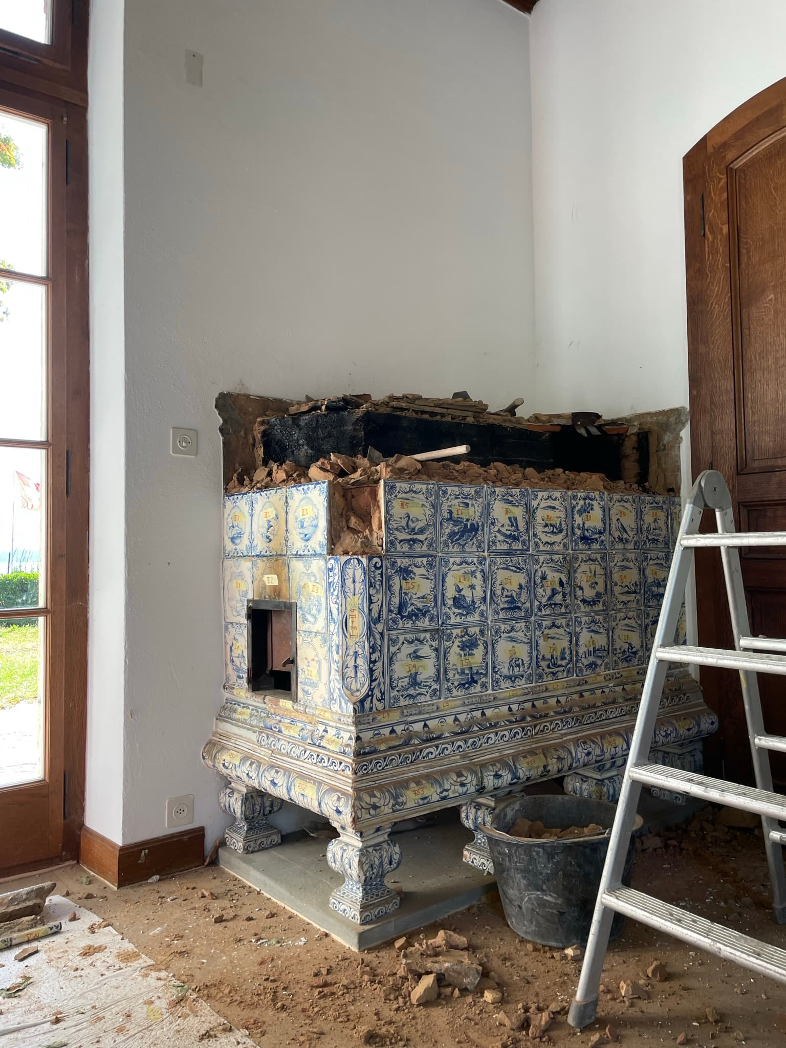 Teilweise abgebauter blau-weisser Kachelofen in einem hellen Raum