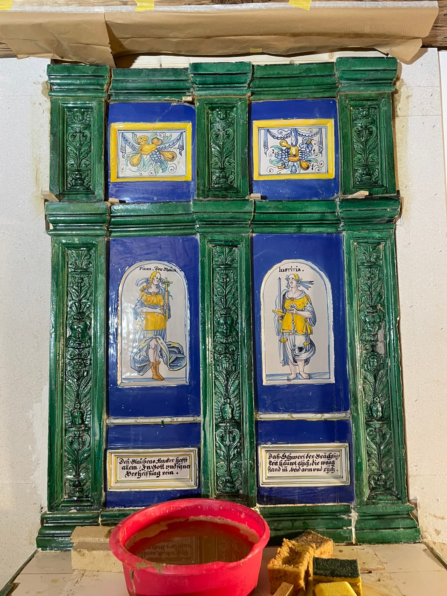 Frontansicht des grün-blauen historischen Figurenofens während der Restaurierung