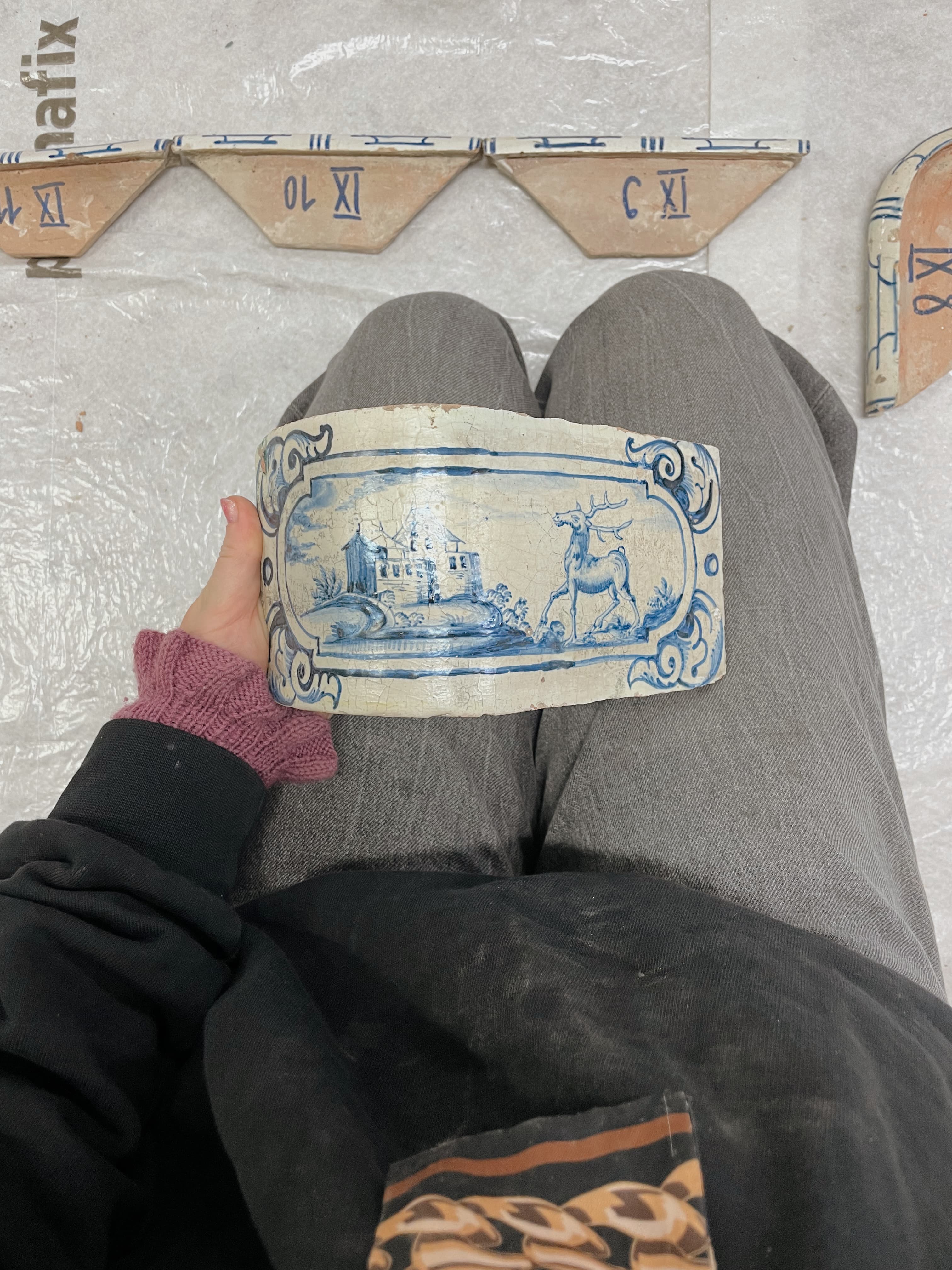Hand hält eine blau-weiss bemalte Kachel mit Landschaftsmotiv